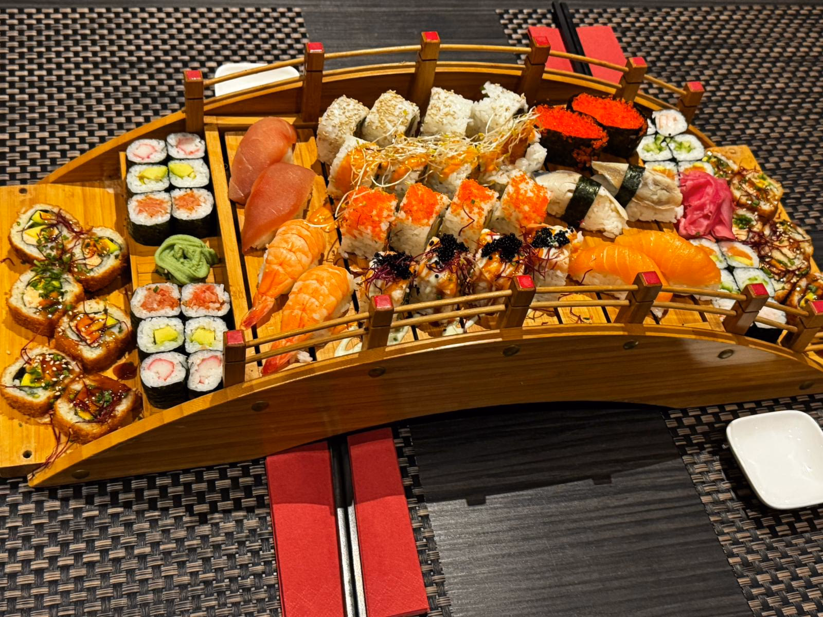 Sushi-Platte auf einer Holzbrücke: Maki, Nigiri, Inside-Out-Rollen und Sashimi